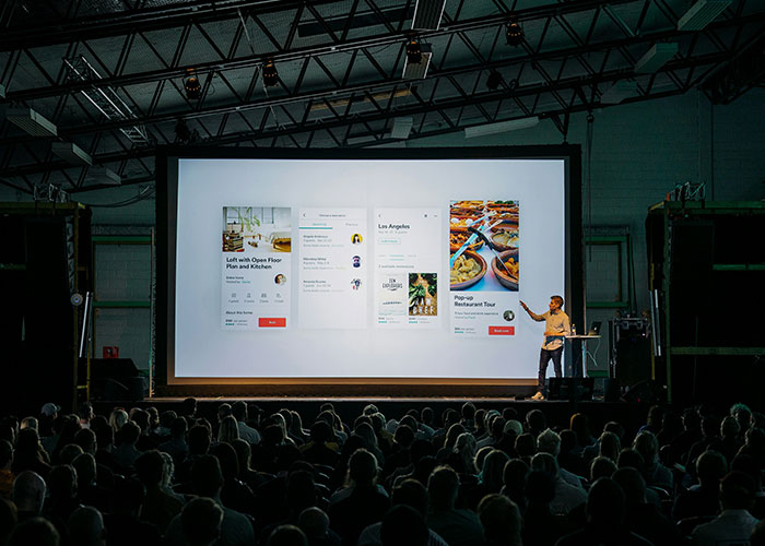 Presenter pointing at large screen with work-related content in front of audience illustrating colossal mess-ups at work.