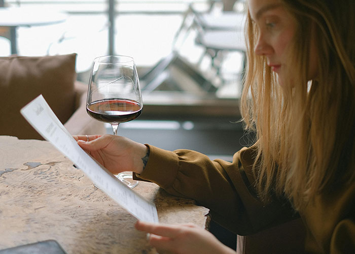 Woman reading a document at a table with a glass of red wine, illustrating a colossal mess-up at work scenario.