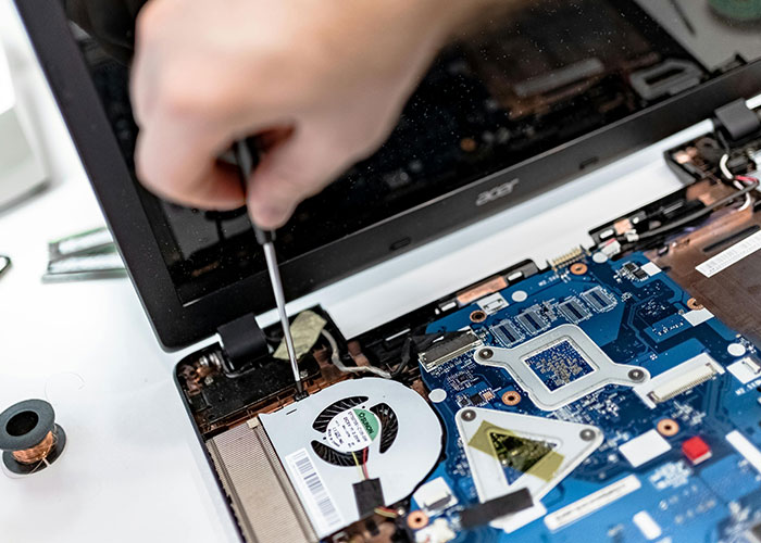 Person repairing a laptop motherboard with a screwdriver, illustrating work mess-ups and technical mistakes at work.