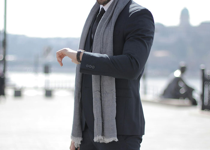 Man in suit and scarf checking watch outdoors, illustrating a work mess-up or time management error.