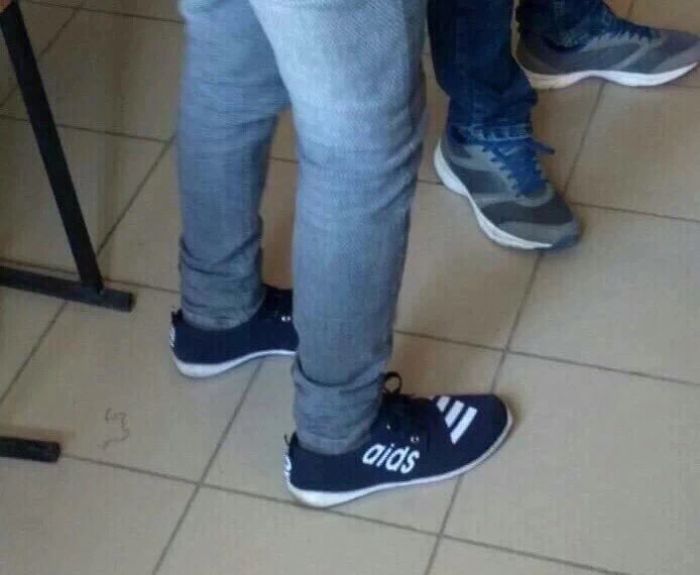 Rip-off sneakers with a misspelled sports brand logo worn by a person standing on a tiled floor, highlighting brand knockoffs.