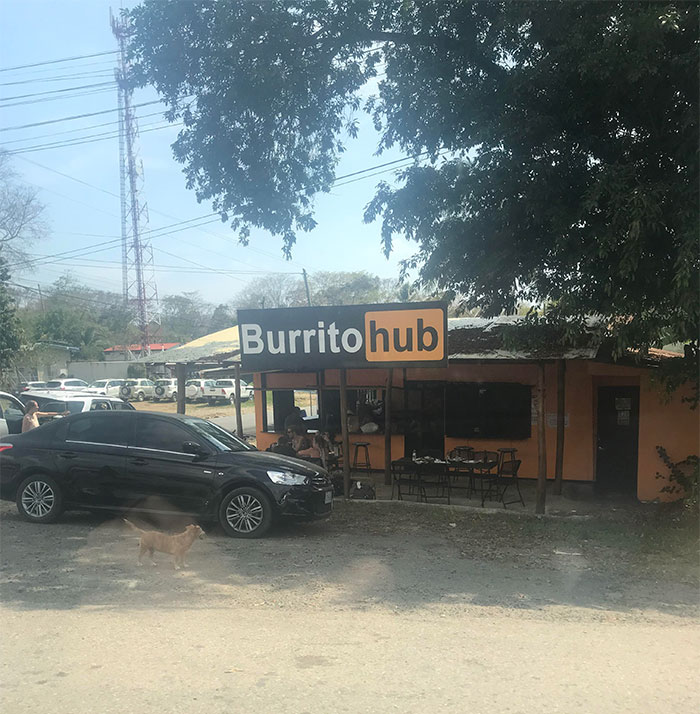Outdoor view of a restaurant named Burrito hub with a black car and a dog in front, showcasing bad rip-offs of brands.