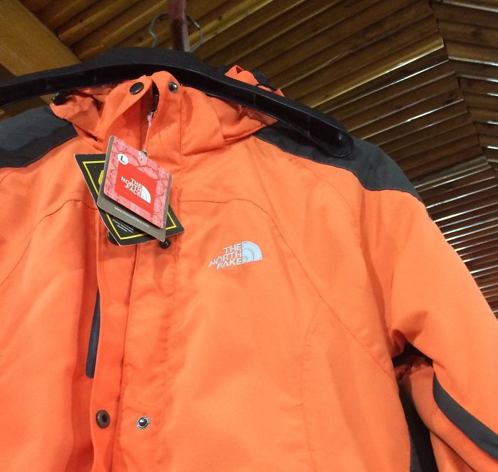 Orange jacket with a rip-off logo The North Fake hanging on a black hanger showcasing bad rip-offs of brands