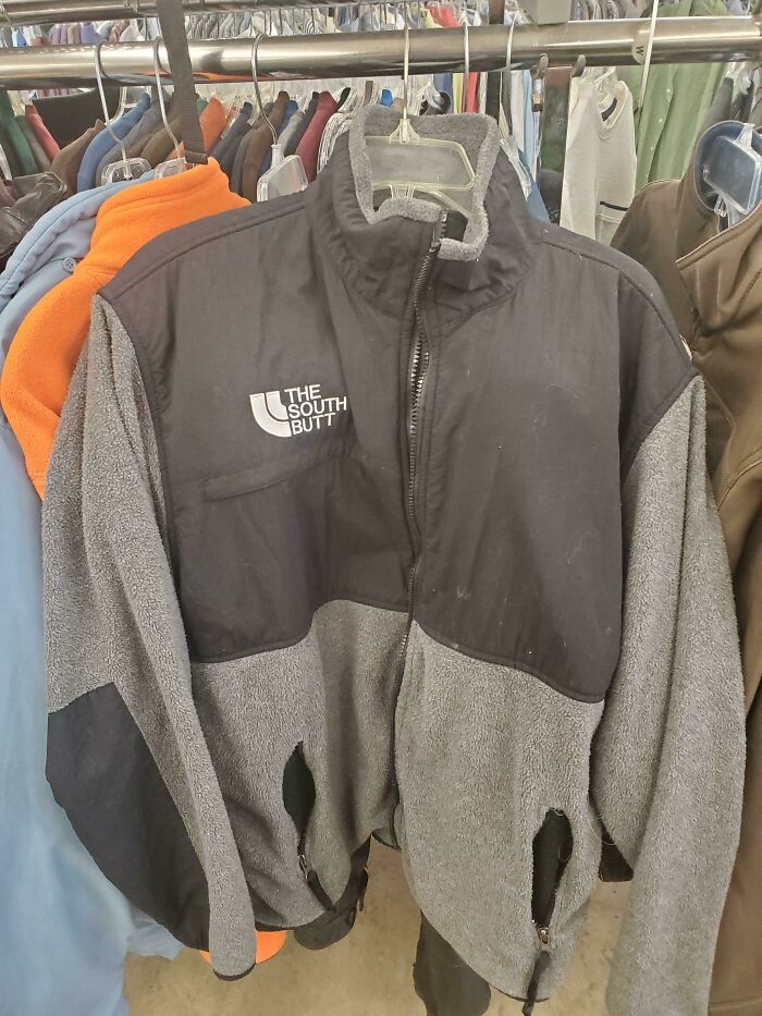 Black and grey fleece jacket with a hilariously bad rip-off logo mimicking well-known brands on a clothing rack.