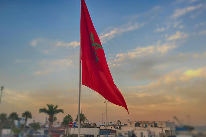 Red Moroccan flag waving against a sunset sky, representing unique historical facts.