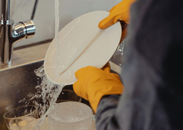 Person washing dishes with yellow gloves in a kitchen sink, illustrating a new job mistake and quitting theme.