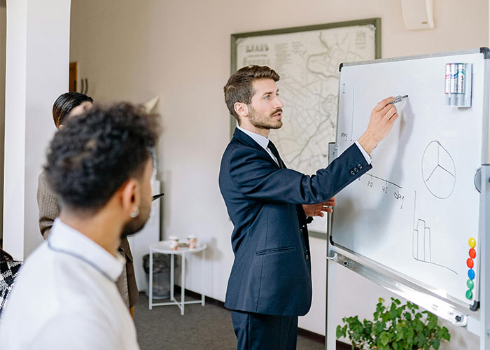 Man in suit explaining charts on whiteboard during a meeting, illustrating moments when people realized new job was a mistake.