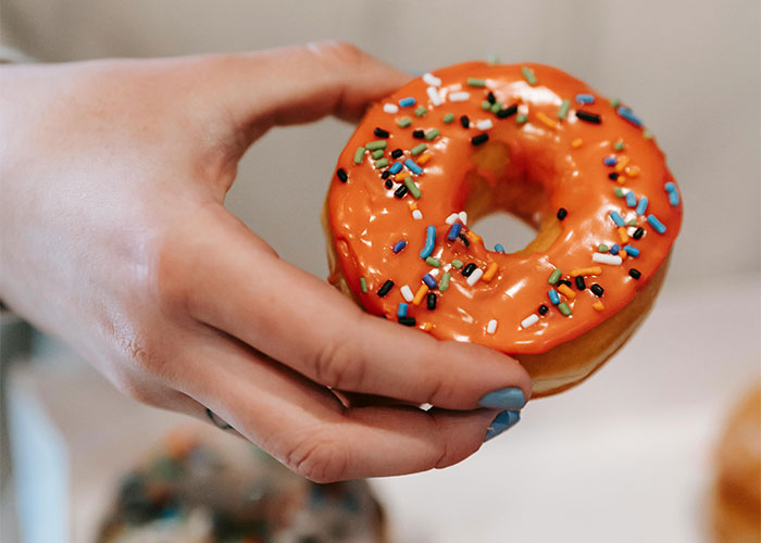 Hand holding a donut with orange icing and colorful sprinkles, symbolizing people leaving new jobs after mistakes.