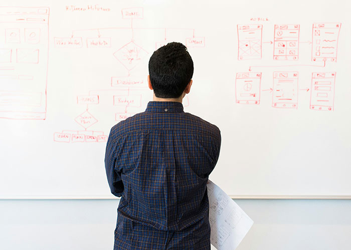 Man in a checkered shirt reviewing complex flowcharts on a whiteboard, symbolizing realizing a new job was a mistake.