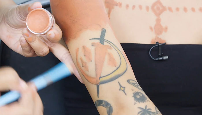 Makeup artist concealing a large tattoo on an arm with cover-up makeup.