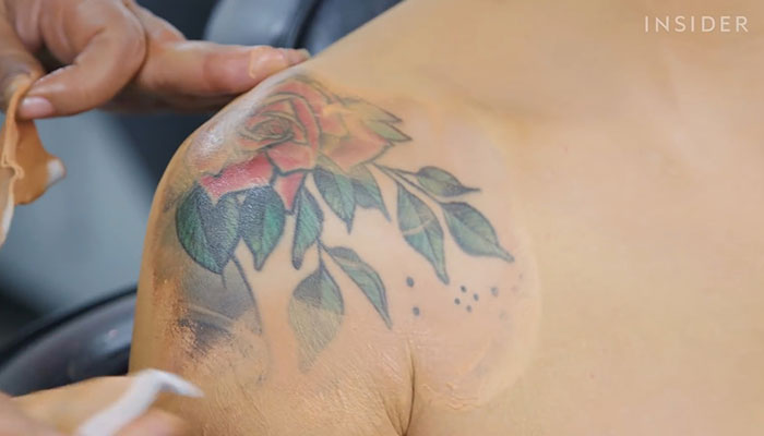 Makeup artist covering a large rose shoulder tattoo with concealer.