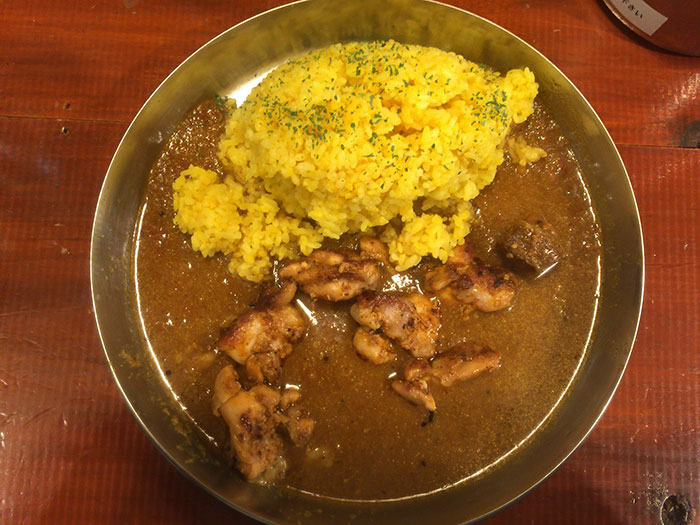 Plate of curry with yellow rice and grilled chicken pieces, representing stereotypes about people’s home countries in a humorous way.