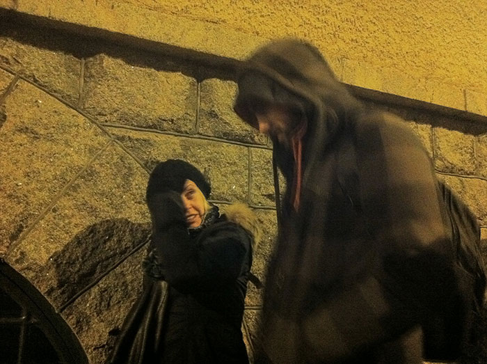 Two people in hooded jackets laughing outside against a stone wall illustrating stereotypes about home countries.