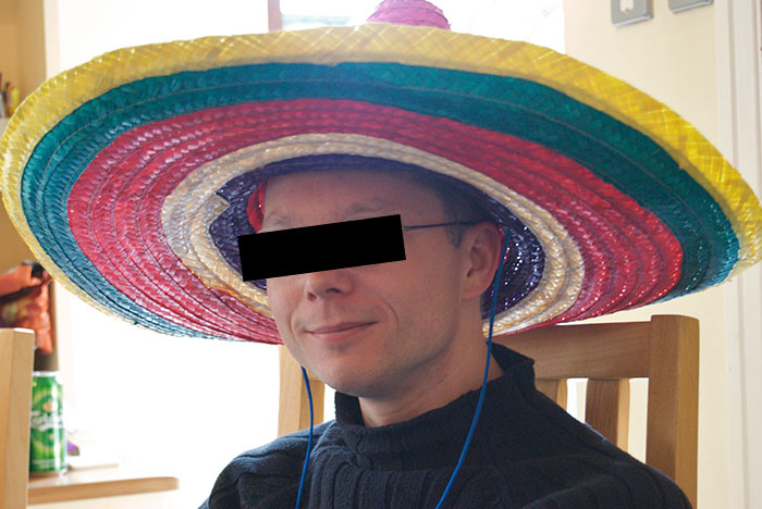 Man wearing colorful sombrero indoors representing stereotypes about people’s home countries with humor and cultural elements