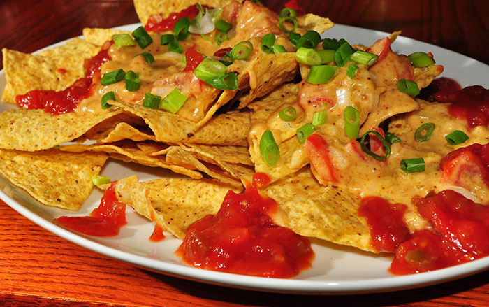 Plate of nachos topped with melted cheese, salsa, and chopped green onions, illustrating food stereotypes about home countries.
