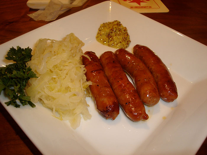 Plate with grilled sausages, sauerkraut, mustard, and parsley, illustrating funny stereotypes about people’s home countries.