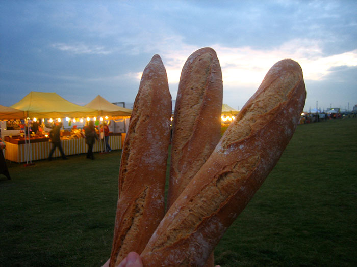 Three baguettes held up at an outdoor market during dusk, highlighting stereotypes about people’s home countries.