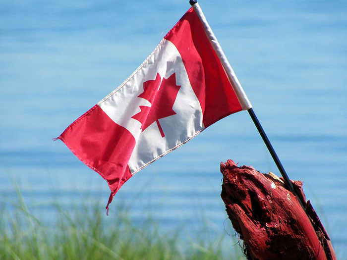 Canadian flag waving near water, illustrating stereotypes about people’s home countries in humorous context.