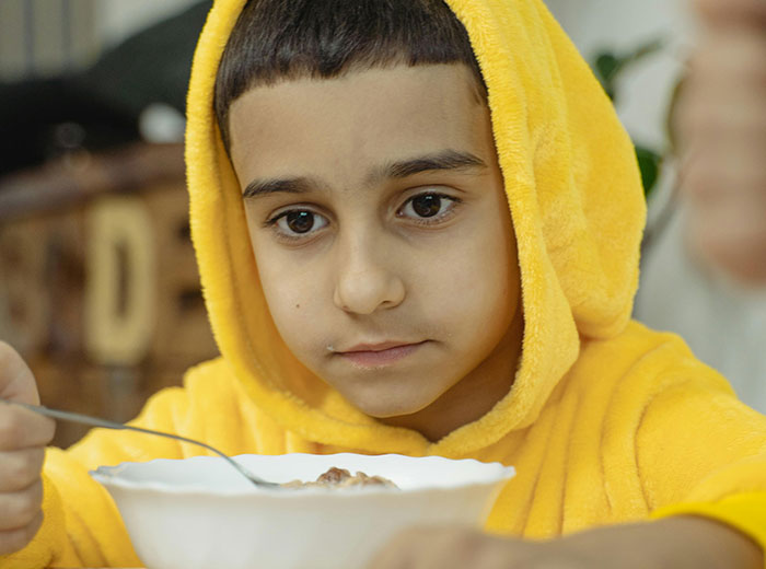 Young boy in a yellow hoodie eating from a bowl, illustrating unusual house rules that left guests grimacing.