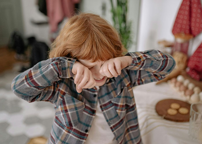 Young child rubbing eyes in a cozy home setting, illustrating concepts related to unethical parenting hacks and child manipulation.