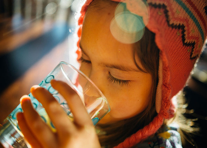 Child wearing a colorful knit hat drinking from a glass, illustrating unethical parenting hacks and manipulation techniques.