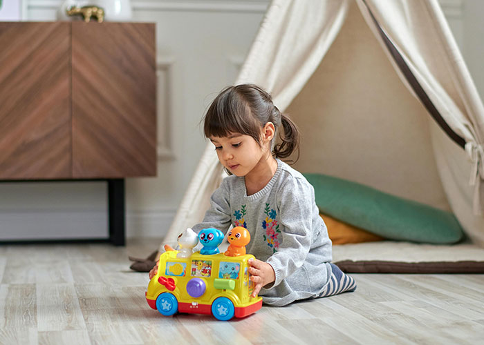 Young girl playing with a colorful toy bus indoors illustrating unethical parenting hacks with manipulative kids.