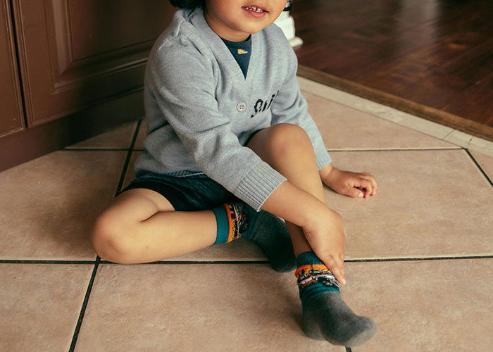Young child sitting on tiled floor, wearing a gray sweater and colorful socks, illustrating unethical parenting hacks.