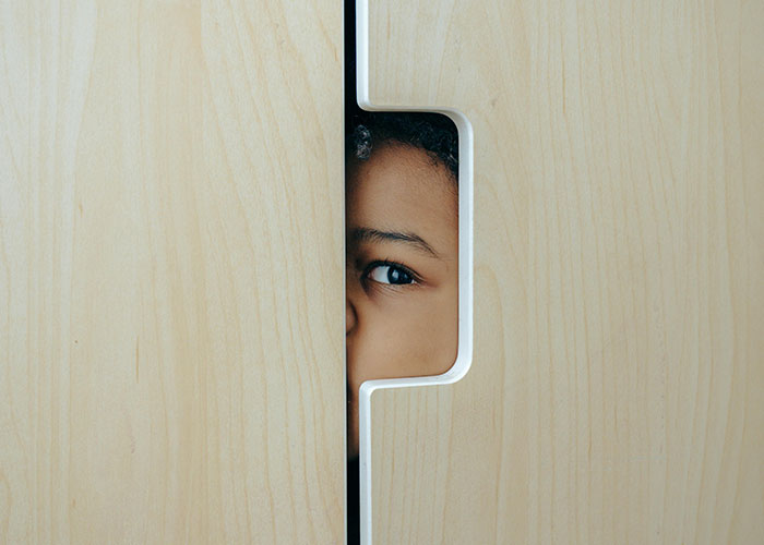 Child peeking through a wooden door crack, highlighting themes of unethical parenting hacks and manipulation.
