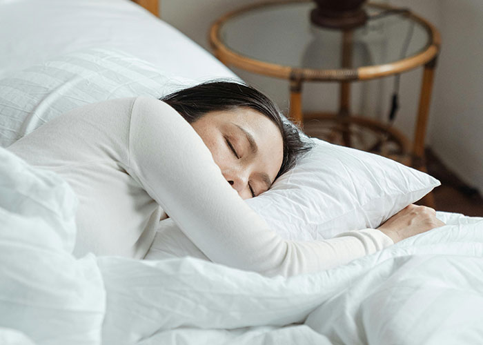 Woman resting on white bed with eyes closed, illustrating a moment of calm in unethical parenting hacks for moms and dads.