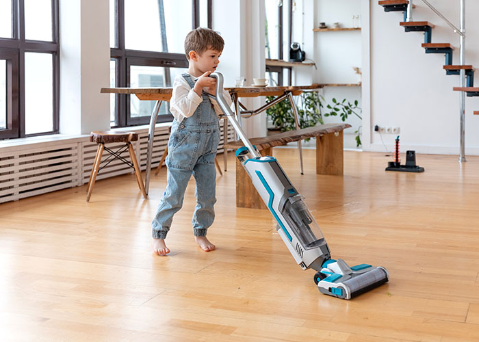 Young boy using a vacuum cleaner indoors illustrating unethical parenting hacks for moms and dads manipulating their kids.