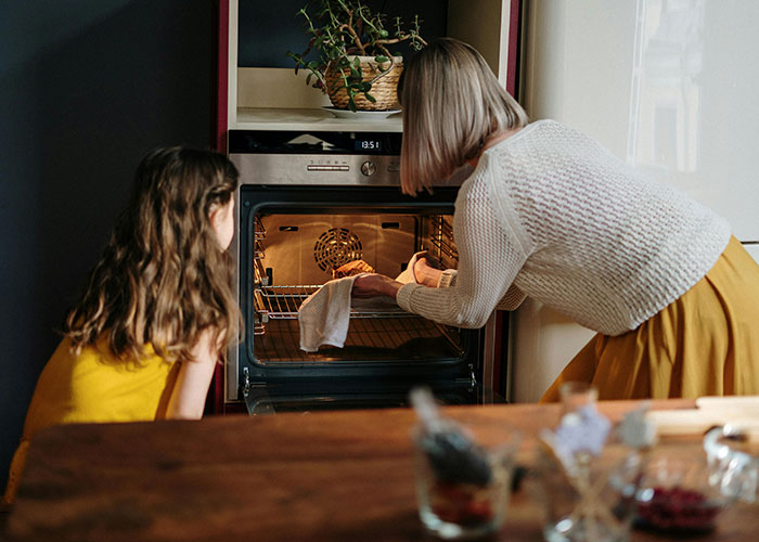 Mother and child using unethical parenting hacks while baking in a cozy kitchen setting with a modern oven.