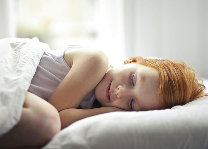 Sleeping red-haired child resting peacefully in bed, illustrating unethical parenting hacks for moms and dads manipulating their kids.
