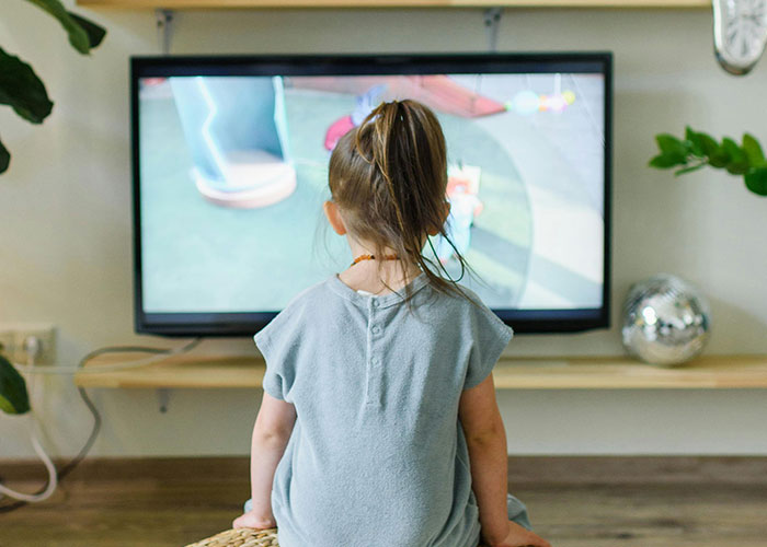Young child watching TV alone in a cozy room, illustrating unethical parenting hacks for moms and dads manipulating their kids.
