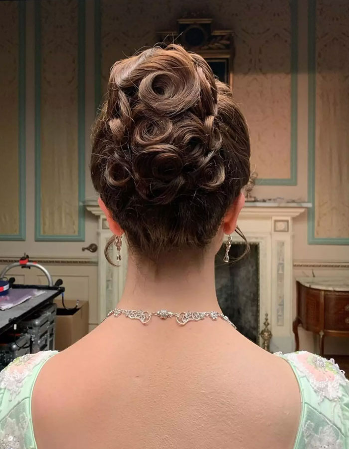 Makeup artist covers tattoo on Claudia Jessie&rsquo;s neck with intricate hairstyle in elegant setting.