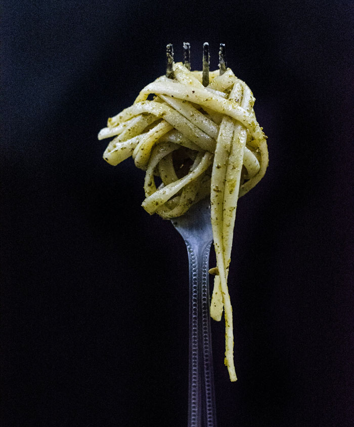 Fork twirling pesto pasta against a dark background, illustrating lifetime supply winnings of food products.