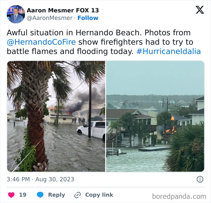 Flooded street with a burning house and firefighters battling flames during severe weather and natural disaster conditions.