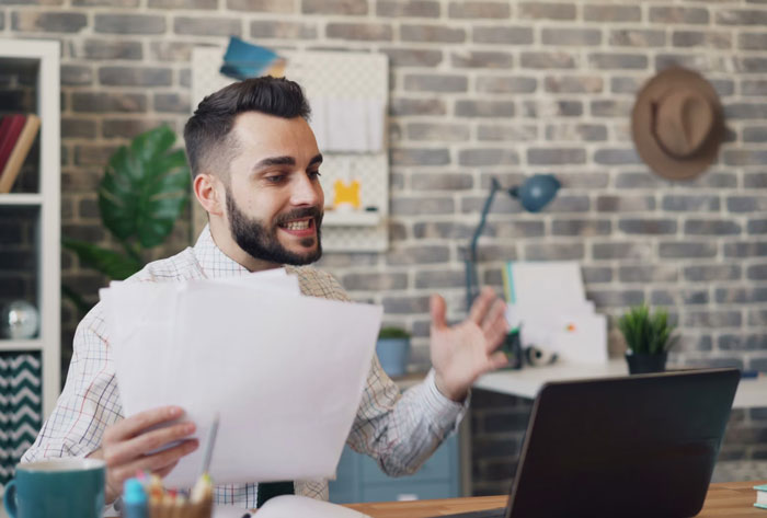 Man showing frustration with computer while holding papers in home office, illustrating embarrassing attempts at understanding computers.