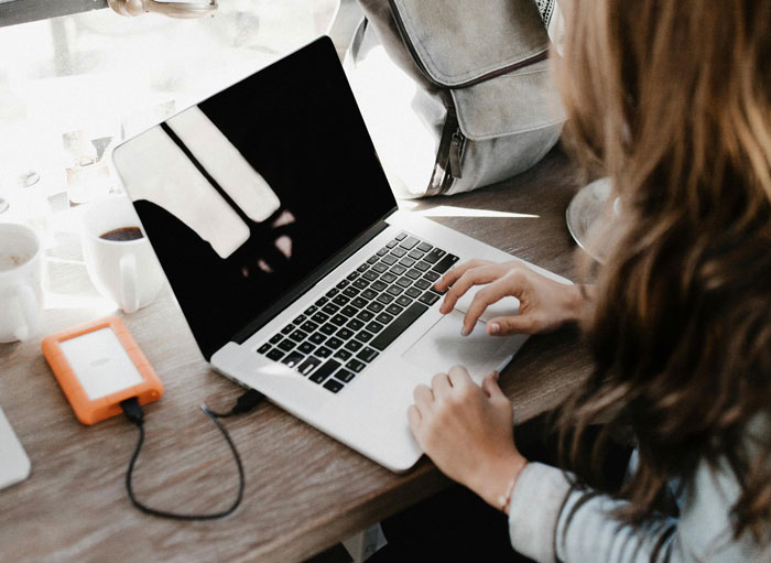 Person using laptop with external hard drive connected, illustrating hilariously embarrassing attempts at understanding computers.