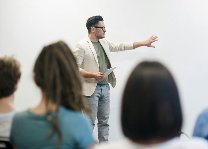 Man in glasses explaining computers to seated audience during a presentation about hilariously embarrassing computer attempts.