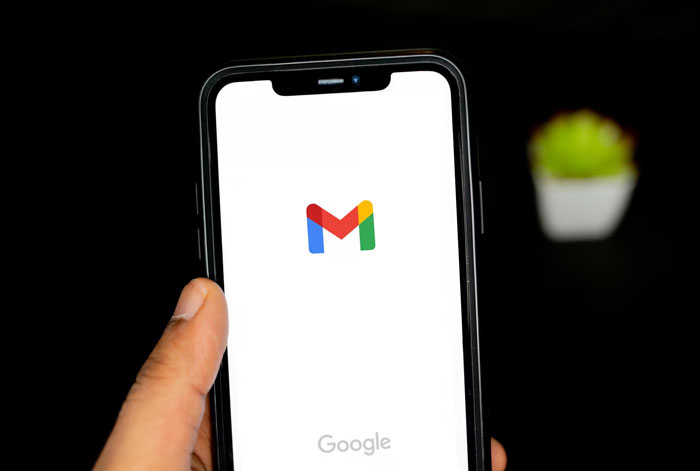 Hand holding smartphone displaying Gmail app loading screen, illustrating funny attempts at understanding computers.