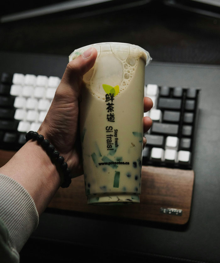 Hand holding a bubble tea cup with pearls in front of a keyboard, illustrating lifetime supply winnings stories.