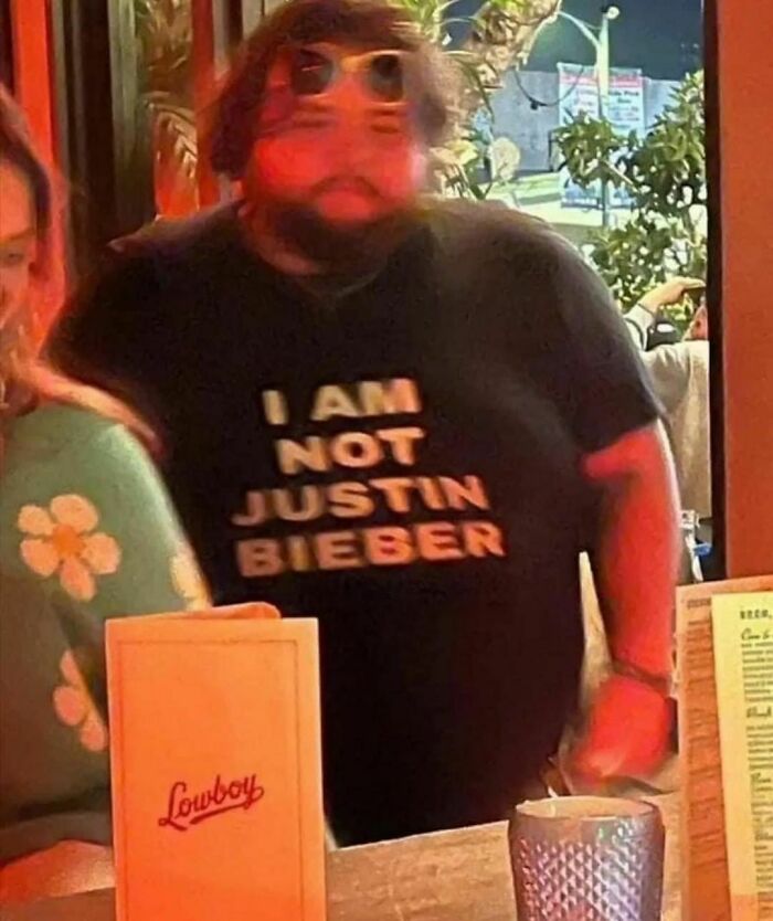 Man with sunglasses on head wearing a shirt that says "I AM NOT JUSTIN BIEBER" at a bar, embodying a hard-hitting style.