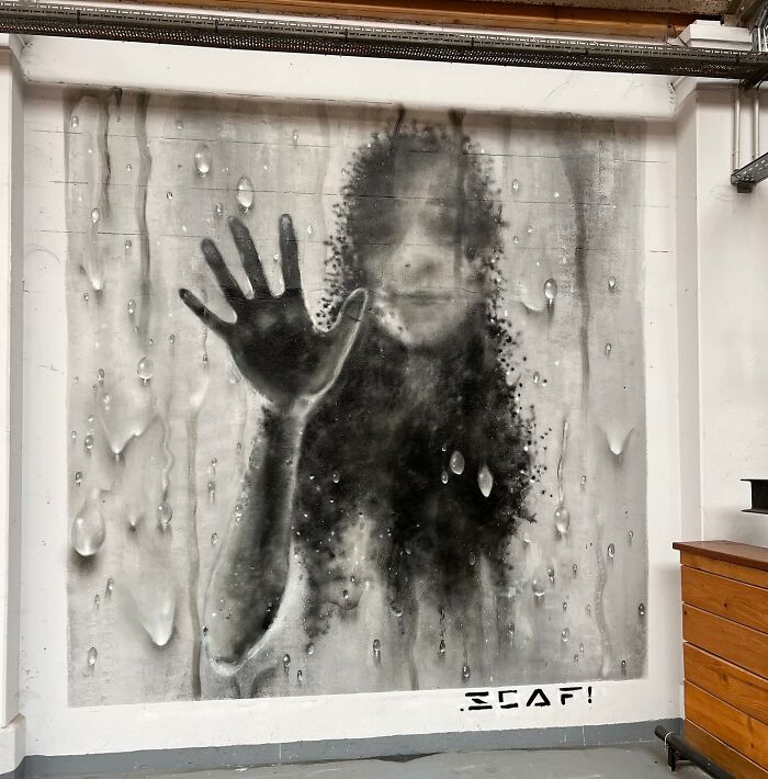 3D graffiti of a person pressing their hand against a rain-covered glass surface, creating a striking visual effect.