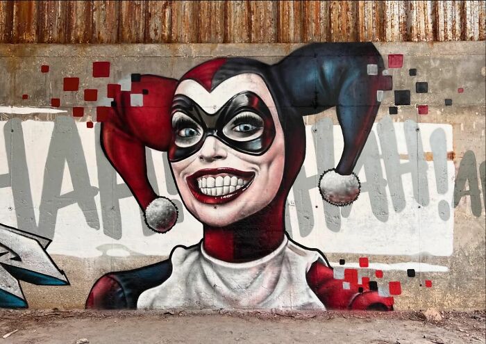 3D graffiti mural of a smiling joker character in red and black costume, showcasing incredible street art by French artist.