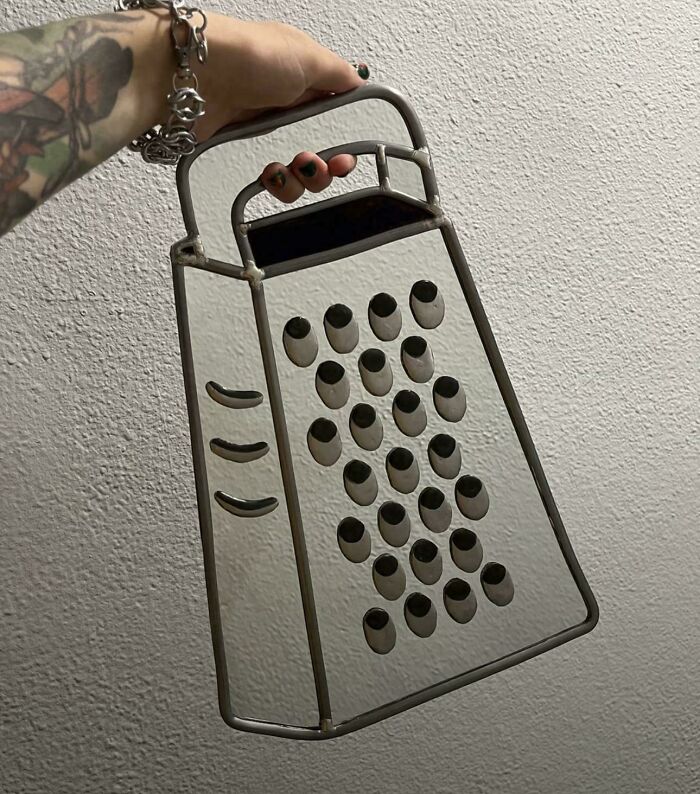 A hand holding a transparent cheese grater frame against a textured wall, causing a confusing optical illusion.