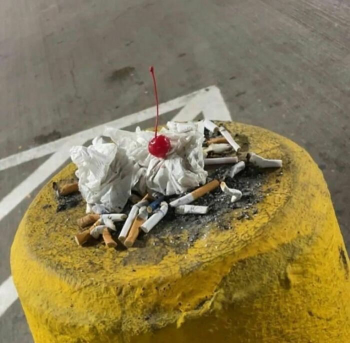 Cigarette butts and crumpled tissues with a cherry on top on a weathered yellow surface in an outdoor setting.
