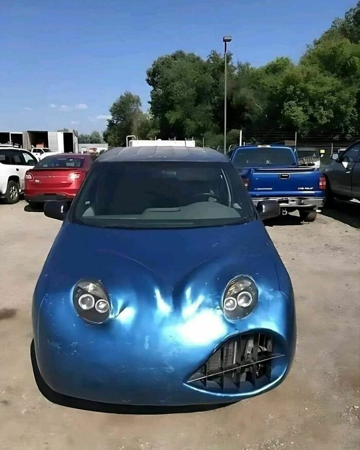 A quirky car with a distorted front design in a parking lot, reflecting sunlight.