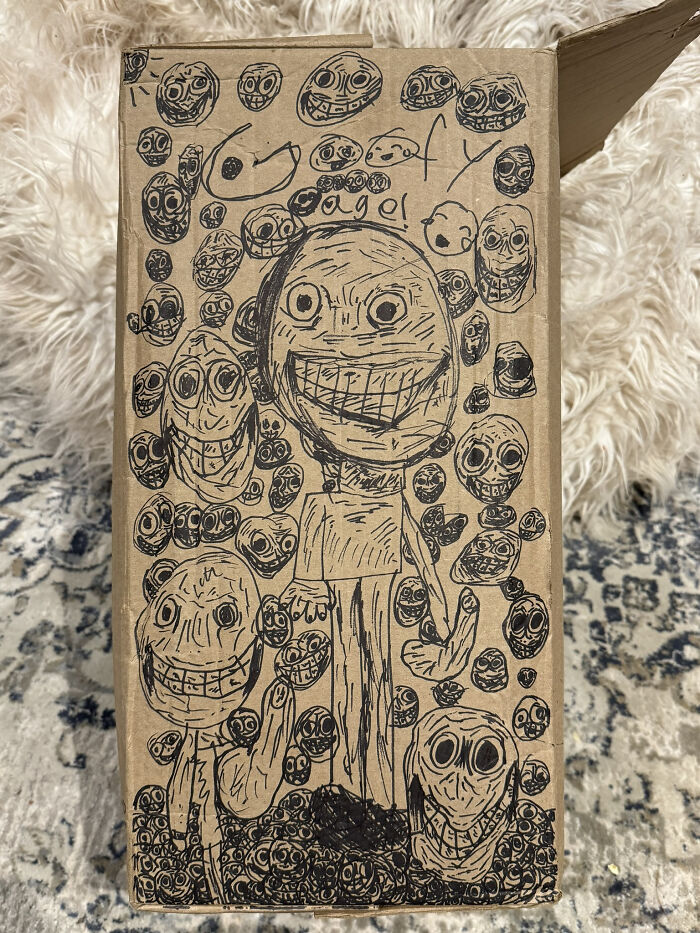 A cardboard box covered in disturbing, hand-drawn creepy images of faces, some grinning, like artwork by kids I babysit.
