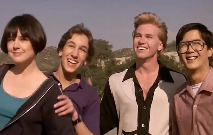 Four friends smiling outdoors on a sunny day, evoking nostalgia and creaking joints memories from past decades.