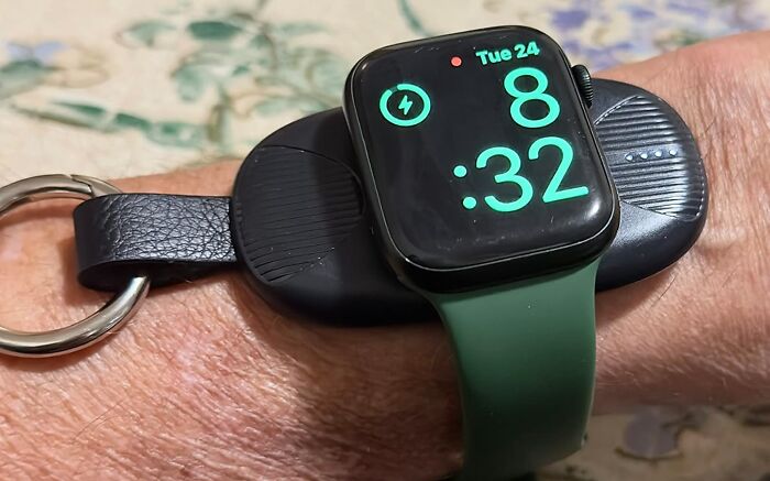 Smartwatch with green strap on a wrist charging on a compact black Amazon tech gadget keychain.